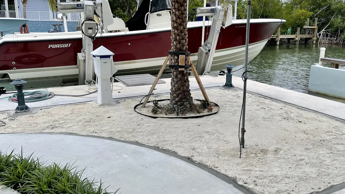 Dockside yard before the install: bare sand inside a poured concrete border, next to a boat lift