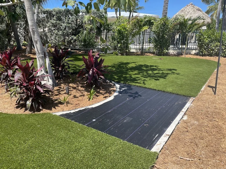 An install in progress: white concrete border along the edge, black weed barrier, and turf laid and glued to the border