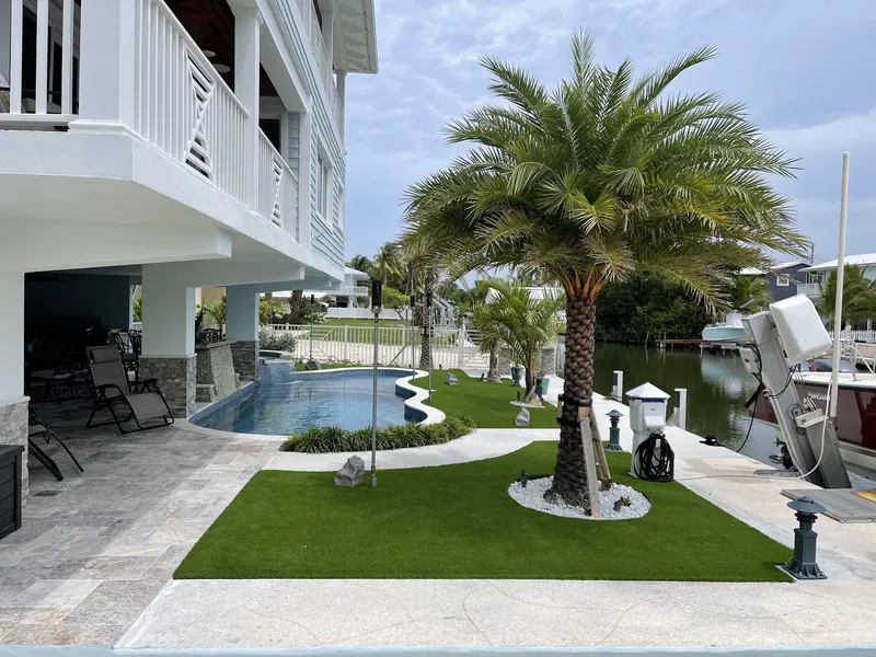 Curved turf lawn around a palm between a pool and a boat dock
