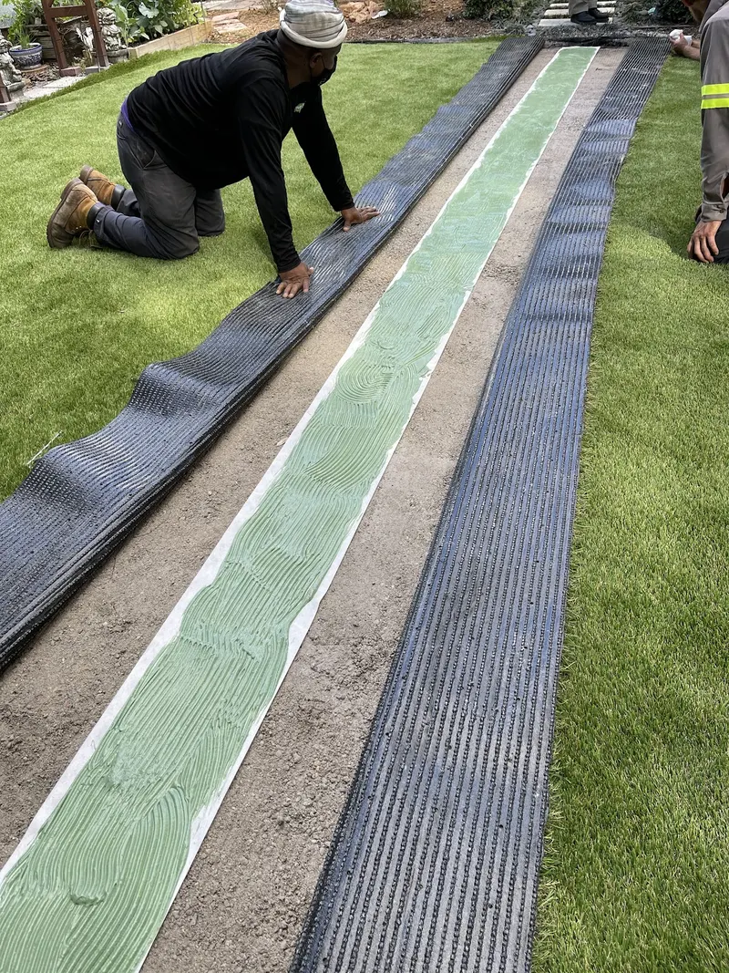 Turf seam being glued along the concrete border, with seam tape laid out