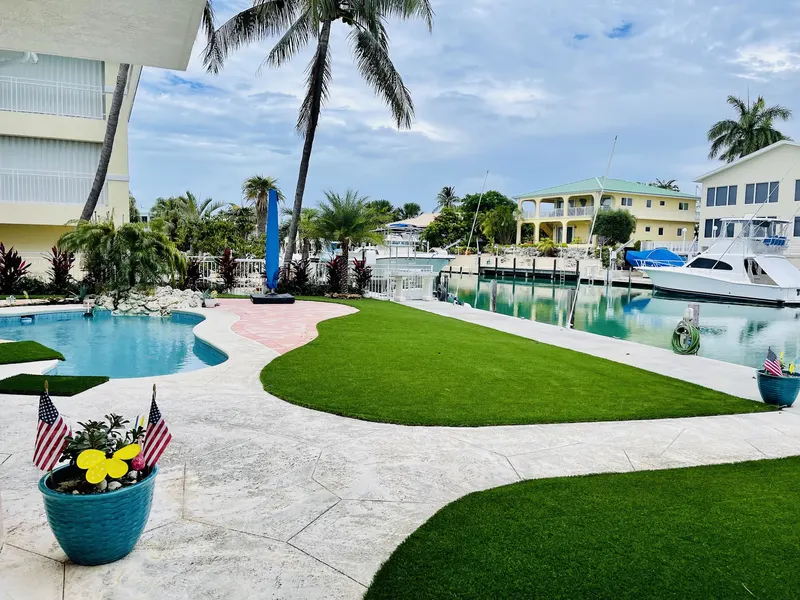 Turf lawn curving between a pool and a canal with boats docked