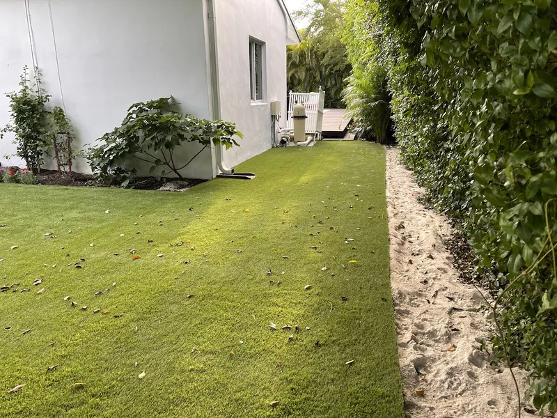 Turf side yard beside a white house and a sand path