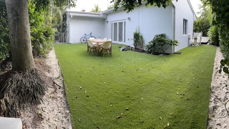 Turf backyard with a patio table beside a white house