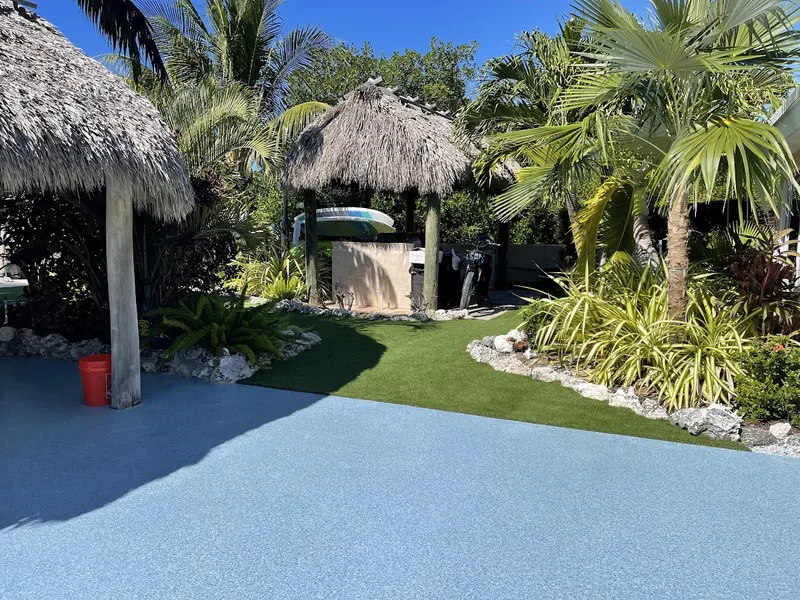 The same backyard after: turf beside the pool deck and tiki huts