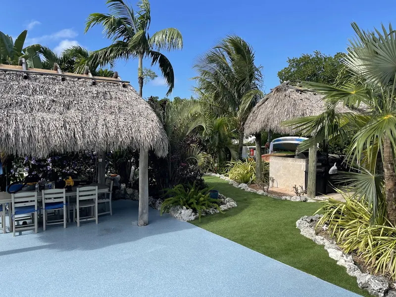 Turf lawn beside a tiki hut and a coral rock garden
