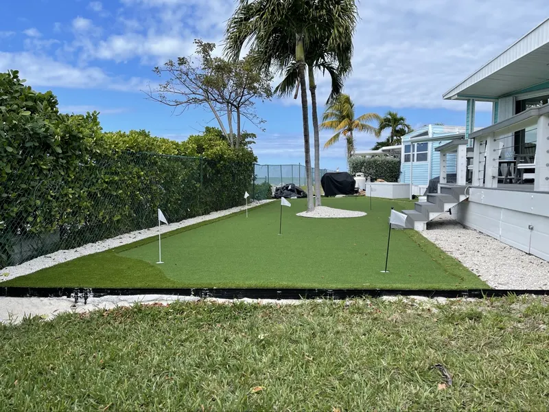 Long putting green with several flags behind a waterfront home