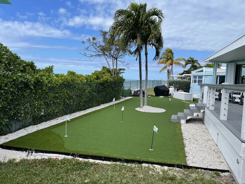 Putting green with flags along a hedge behind a raised home