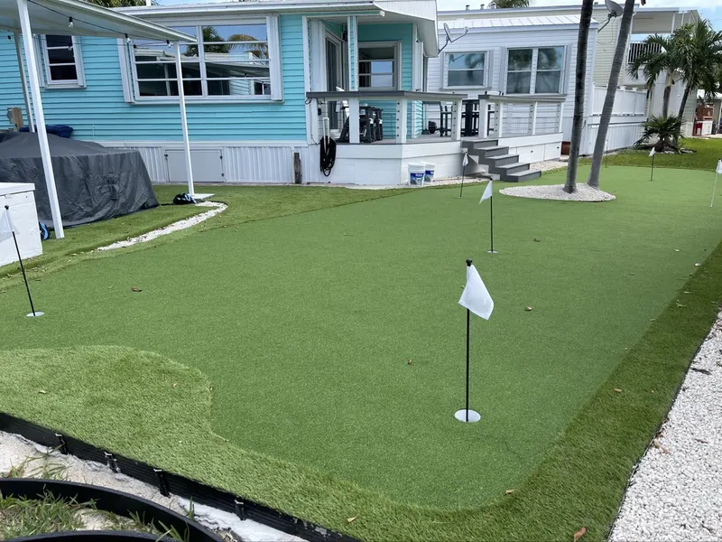 Putting green with fringe and a flag in front of a raised home