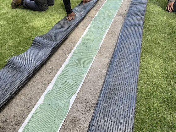 Installer gluing a seam: green glue on seam tape with both turf edges peeled back